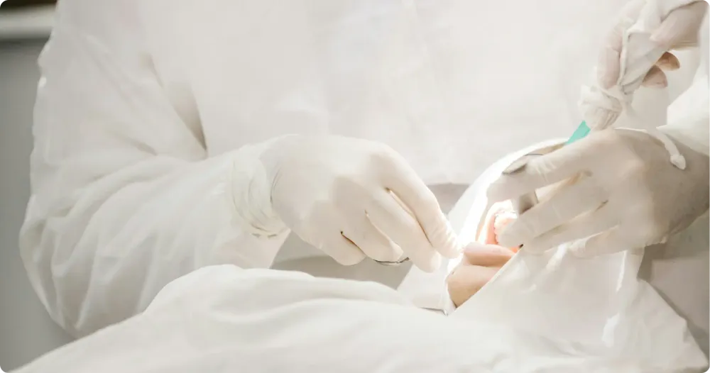 A person wearing a white coat is performing a teeth cleaning procedure on a patient in a dental clinic.