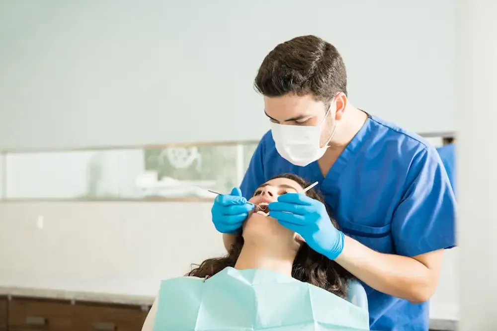 Male dentist in blue scrubs performing a dental procedure on a woman