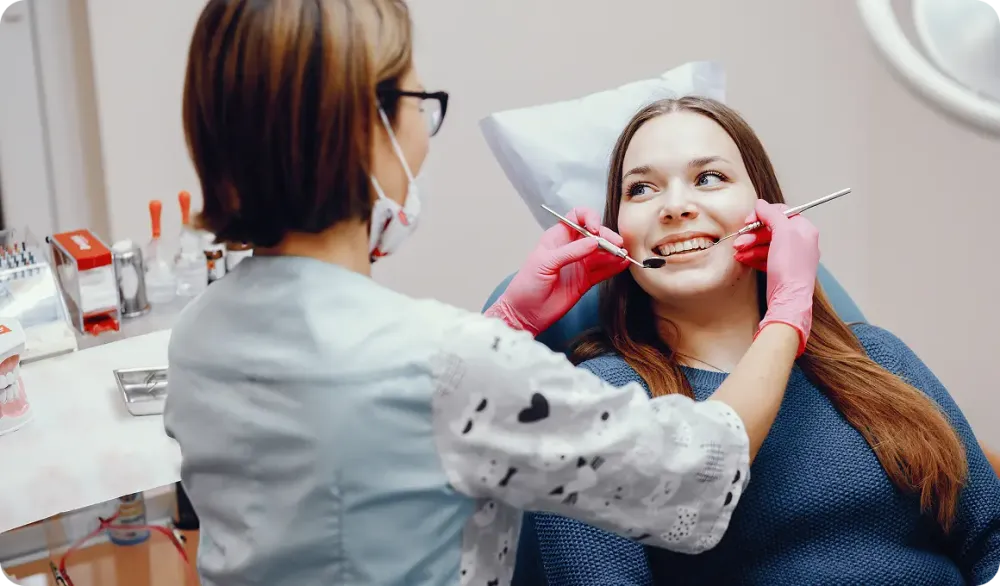 Female dentist examining a smiling patient with dental tools during a check-up.