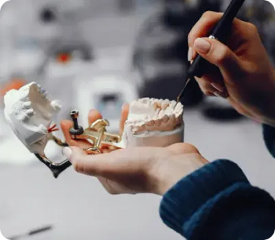 Hands working on a dental prosthesis model with tools in a dental laboratory.