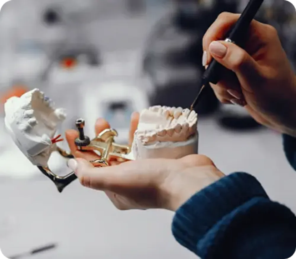 Hands working on a dental prosthesis model with tools in a dental laboratory.