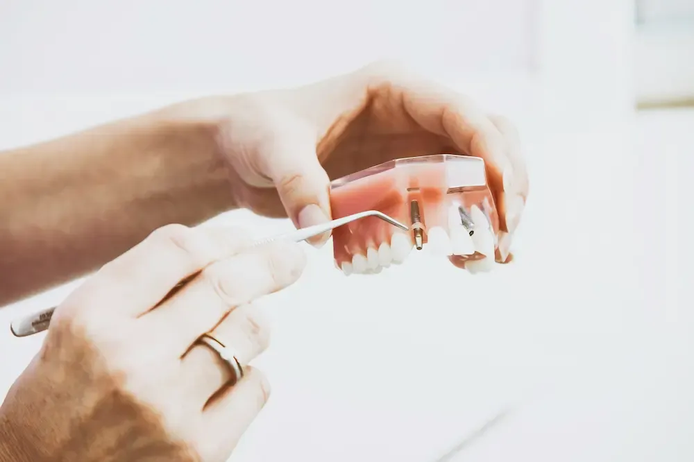 Dentist's hands adjusting a screw on a dental prosthesis with precision tools, performing denture repair or implant maintenance.