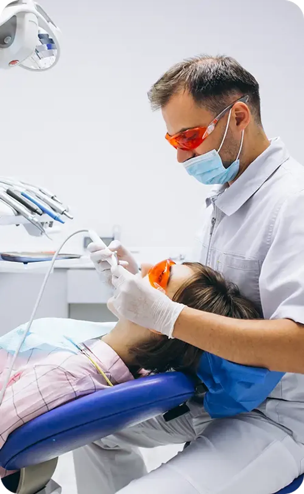 Dentist wearing orange protective glasses performing a dental procedure on a patient.