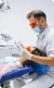 Dentist wearing orange protective glasses performing a dental procedure on a patient.