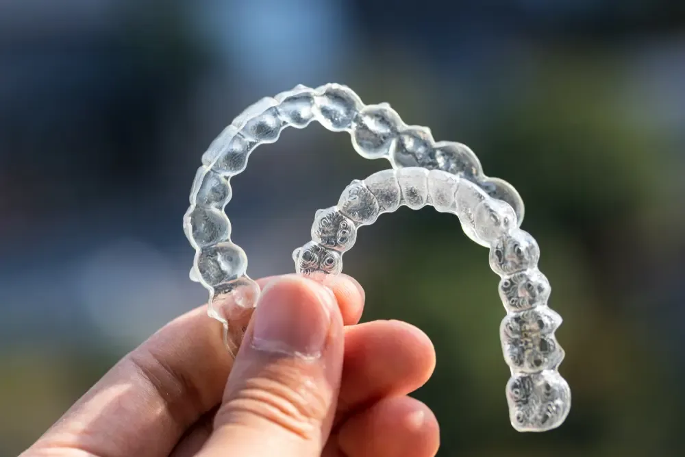 Close-up of clear Invisalign aligners held in hand, showcasing discreet teeth-straightening treatment.