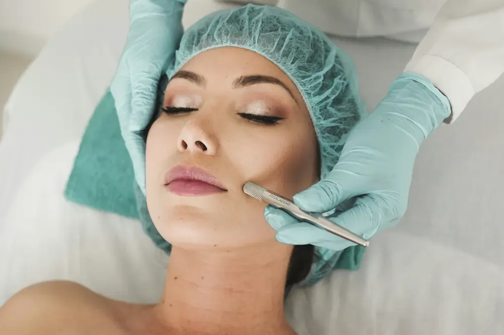 A woman wearing a head cap while a pencil-shaped tool is glided over her face