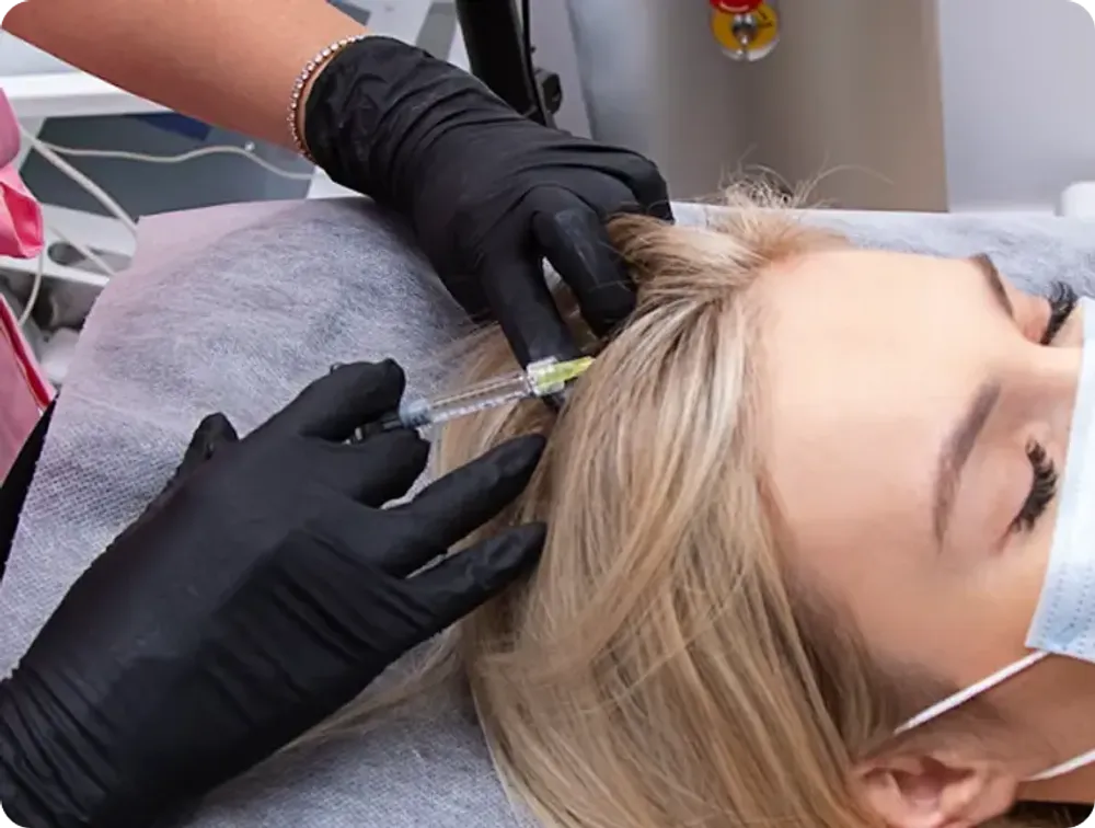 A doctor wearing black gloves injecting a blonde woman's scalp