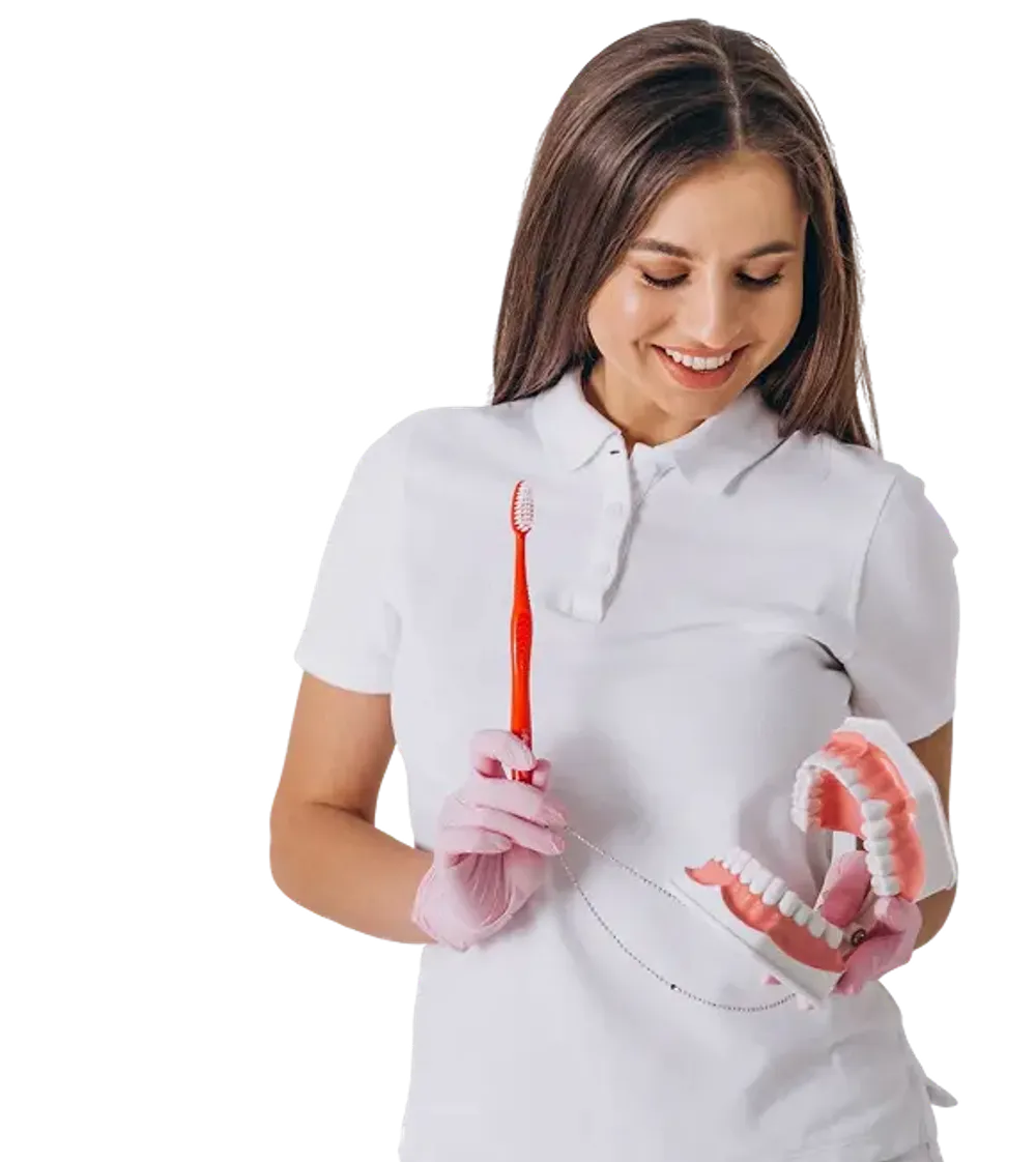 A female dental professional holding a denture in one hand and a toothbrush in the other, wearing pink gloves during a dental cleaning or prosthesis demonstration.